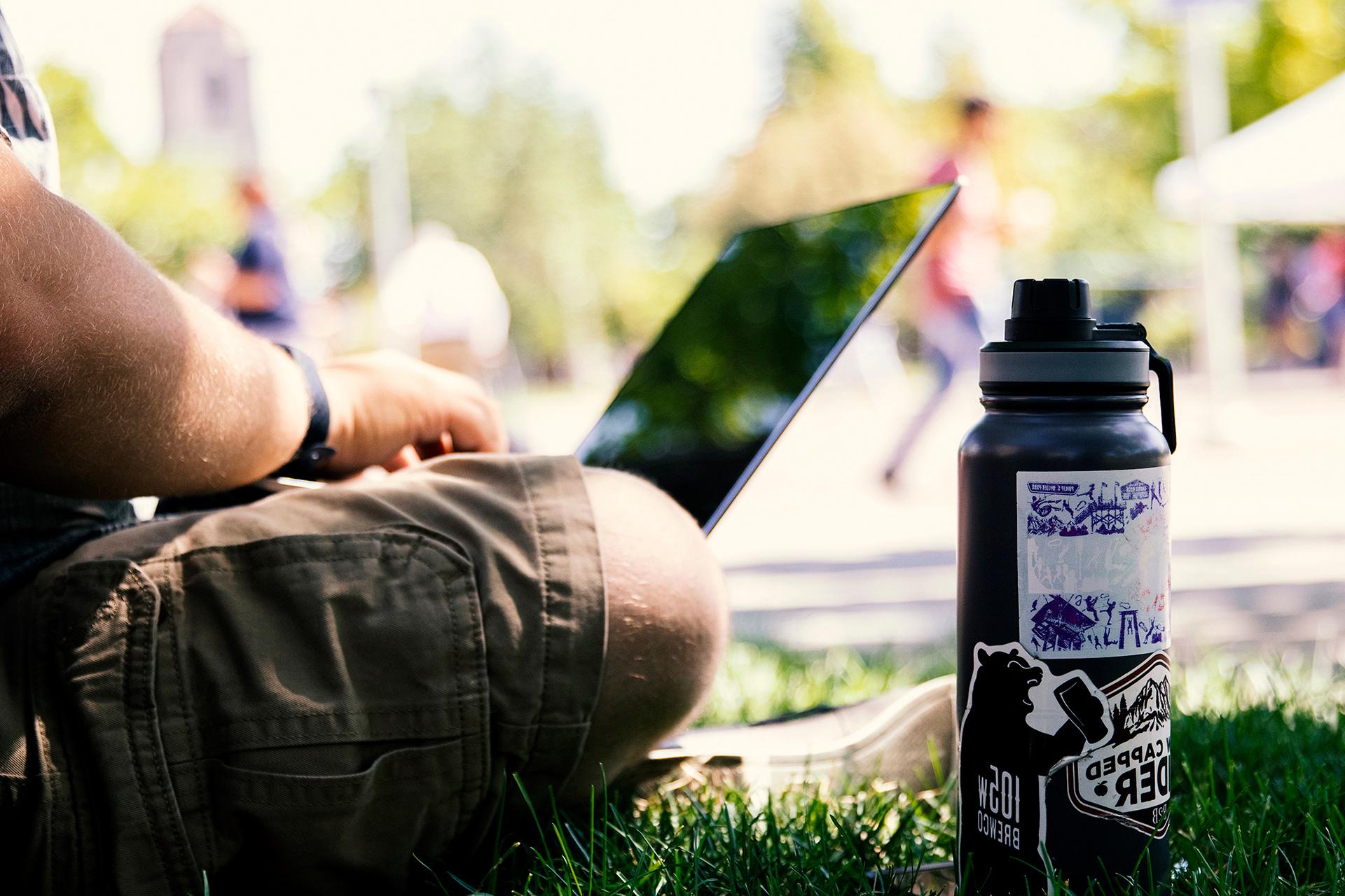 Man sitting on grass with laptop and water bottle