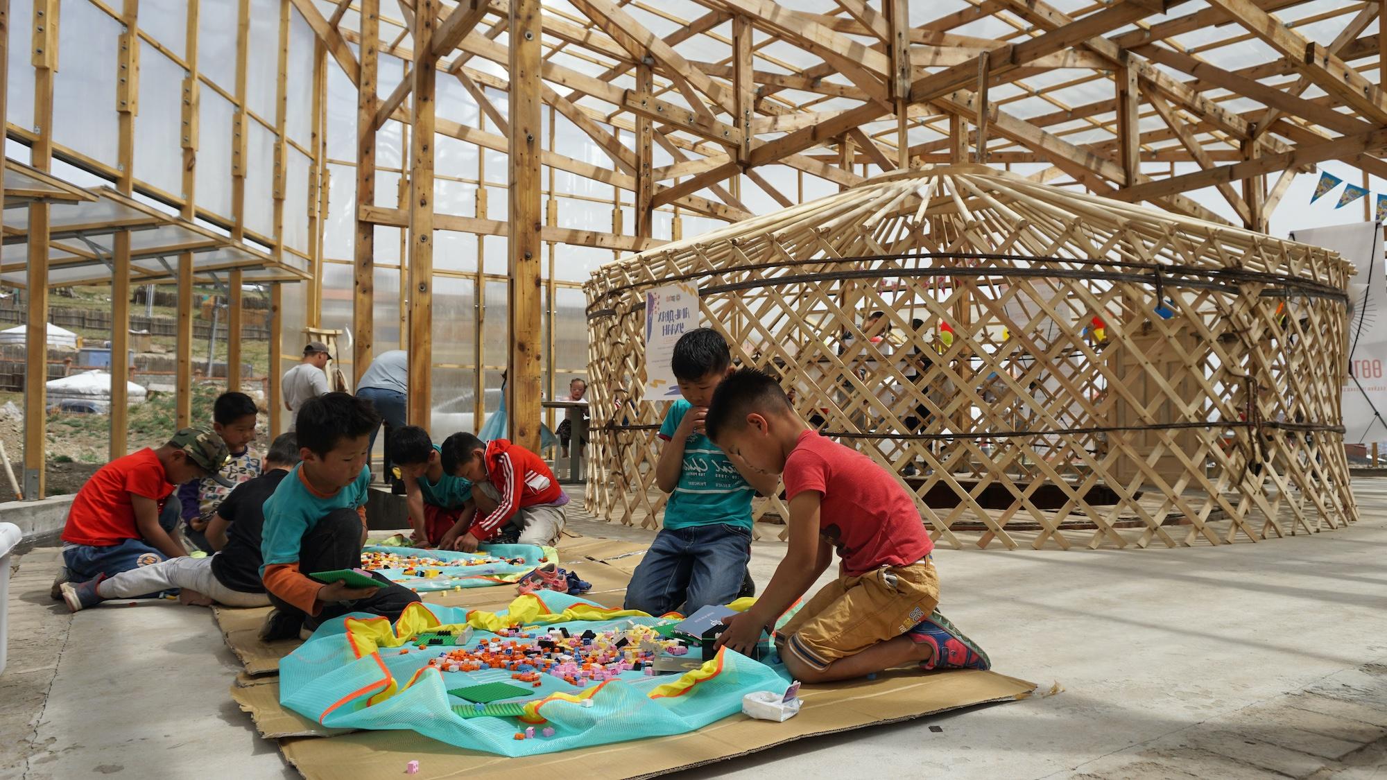 A group of children sit on the floor of a wood-framed and glass-clad structure. 孩子们正在与五颜六色的材料互动.