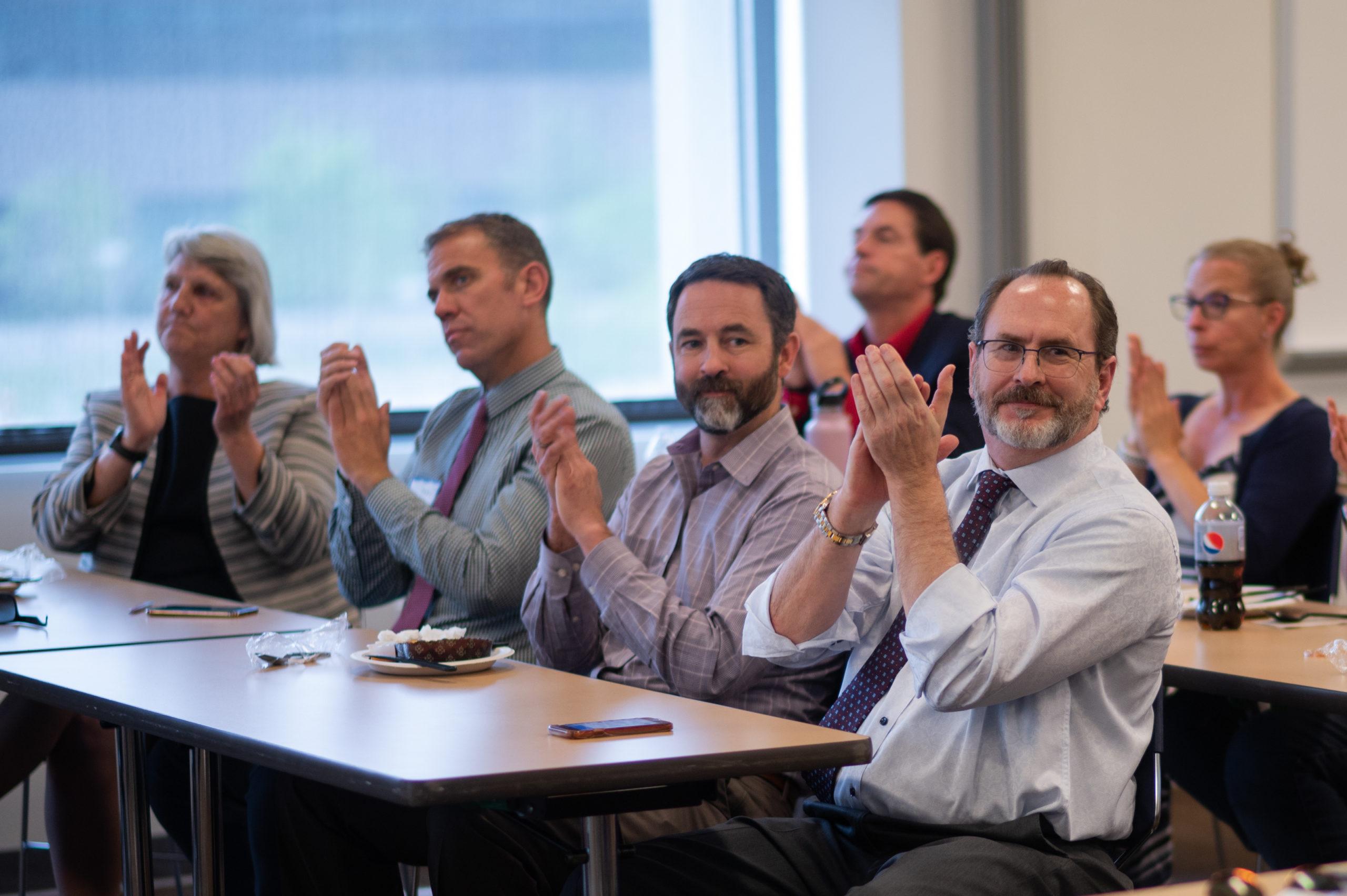 Faculty members clapping at an event.