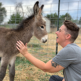 Claire Alfus laughing while petting a baby donkey