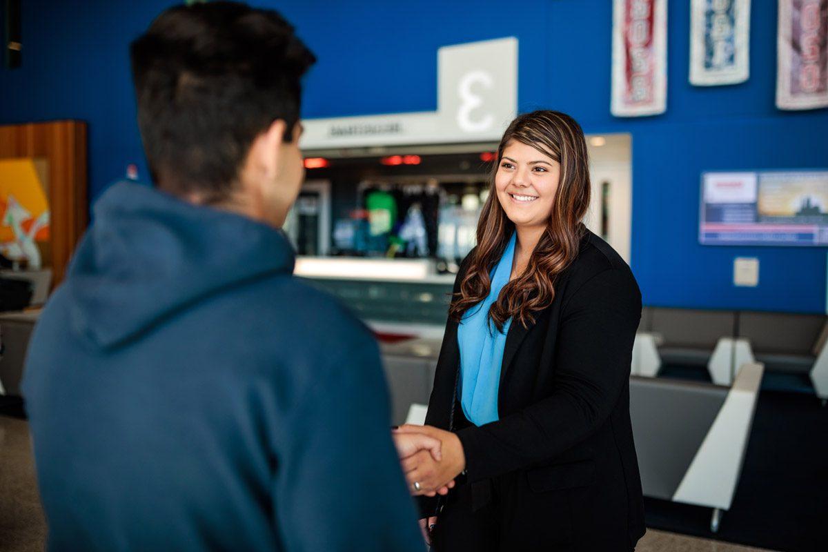 A woman in business attire shaking hands with a male student in the lobby of JSSB