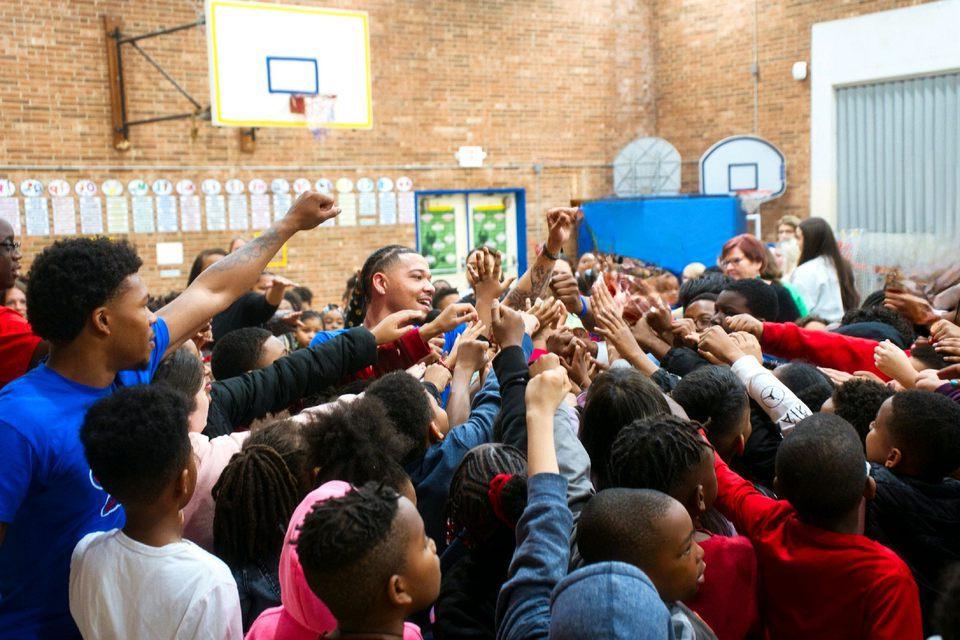 Photo of a group of MISTERs and young students standing in a school gym with their hands up and pointing to the center.